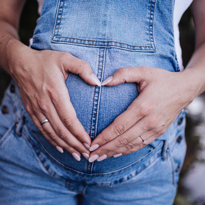 Pregnant woman holding stomach with hands in the shape of a heart